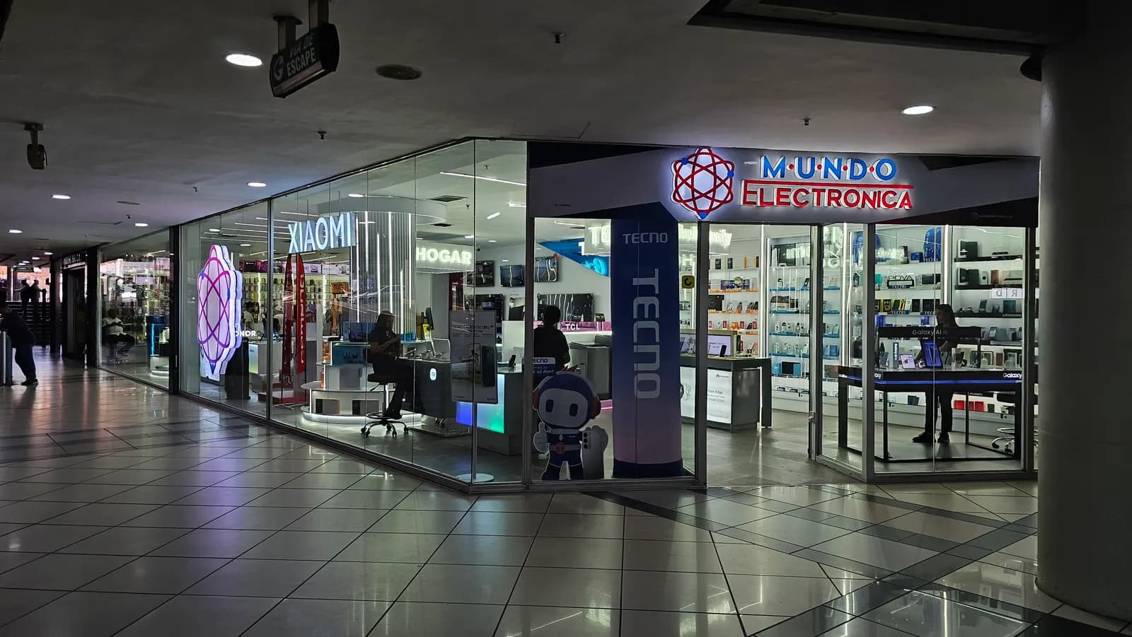 Fachada del local de Mundo Electrónica en El Recreo, con el rótulo iluminado y las vitrinas de piso a techo
