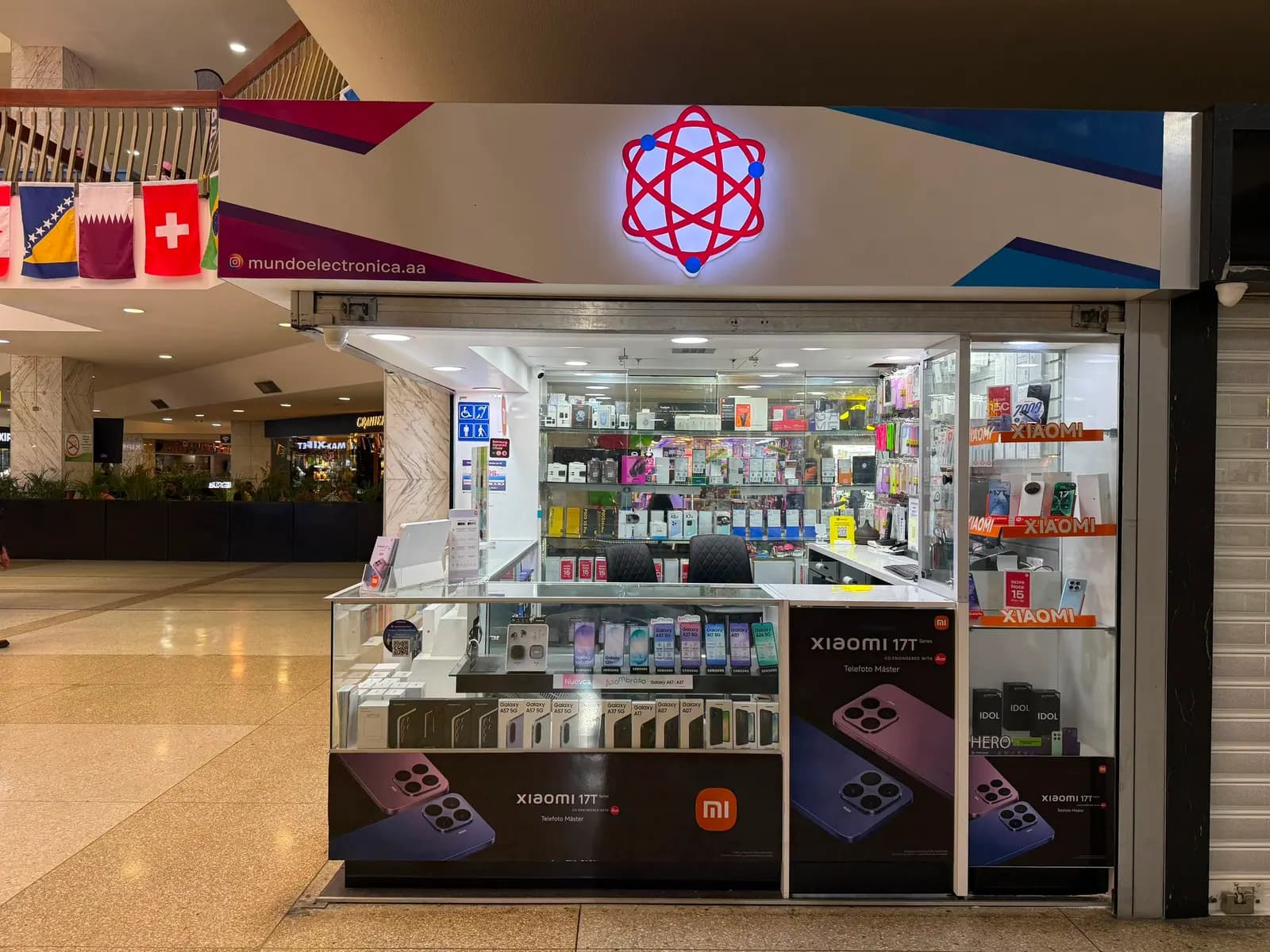Vitrinas del kiosco del CCCT con equipos Samsung Galaxy y Xiaomi exhibidos bajo el átomo de Mundo Electrónica