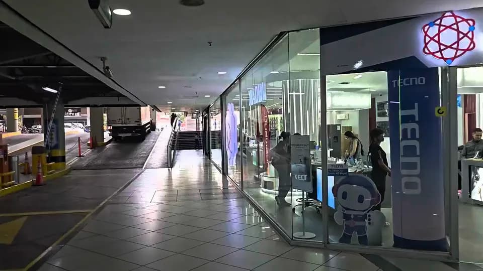 La entrada de la tienda Mundo Electrónica con su logo iluminado y clientes entrando